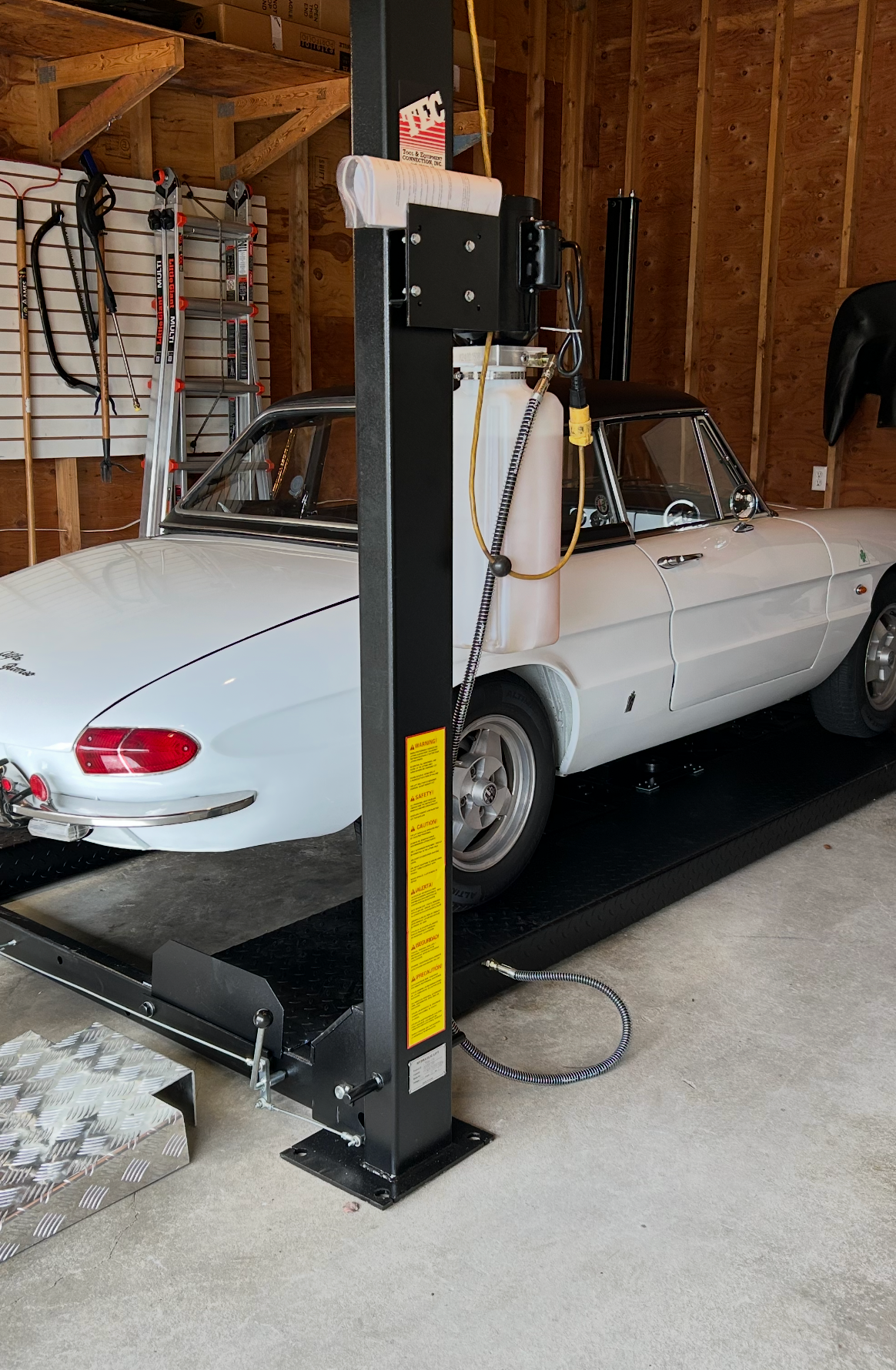 Car lift in a garage with a white convertible car underneath